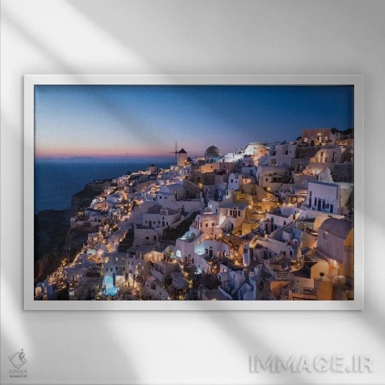تابلو یونان، سانتورینی. روستای اویا در نور پس از غروب میدرخشد و چراغهای شهر به این منظره نماباور جادویی میبخشند اثر برندا ثارپ - نمای قابدار سفید