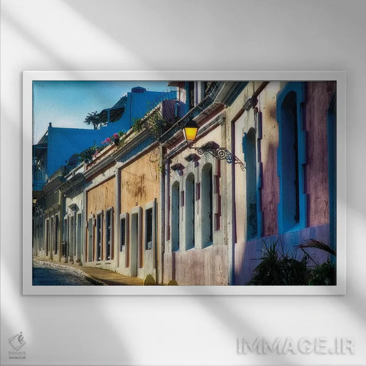 تابلو دکوراتیو خیابان سنگفرش با خانه های رنگی در نور بعدازظهر، سن خوان، پورت… اثر جورج اوزه - نمای قابدار سفید