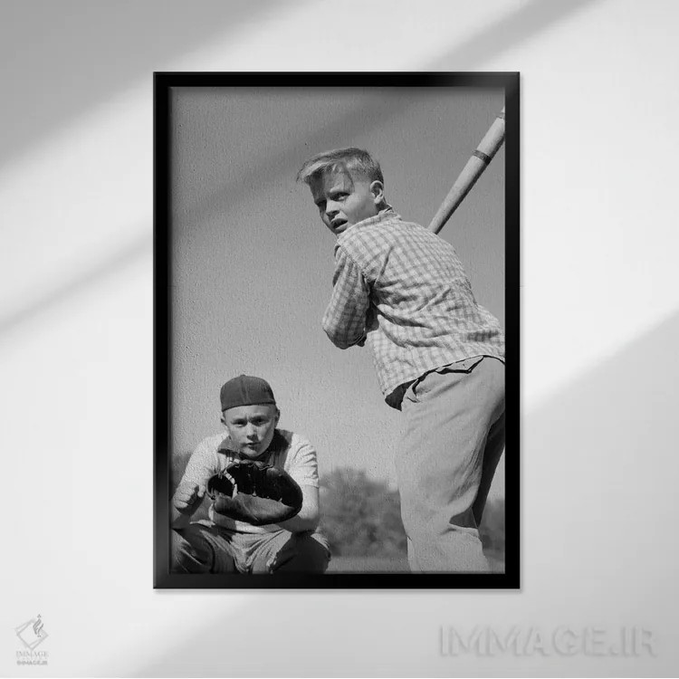 تابلو دکوراتیو نوجوان پسر در حال زدن توپ بیسبال با گیرنده پشت سرش دهه ۱۹۵… اثر تصاویر وینتج - نمای قابدار مشکی