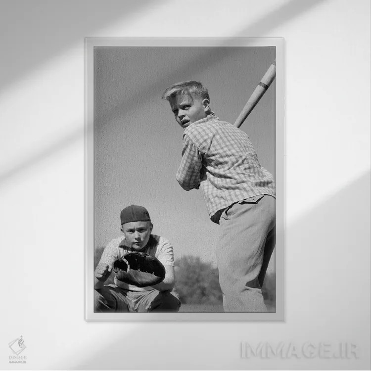 تابلو دکوراتیو نوجوان پسر در حال زدن توپ بیسبال با گیرنده پشت سرش دهه ۱۹۵… اثر تصاویر وینتج - نمای قابدار سفید