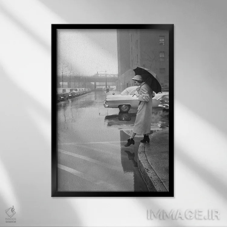 تابلو دکوراتیو دهه ۱۹۵۰ زن با بارانی، کلاه و چکمه، چتر به دست در حال عبور… اثر تصاویر وینتج - نمای قابدار مشکی