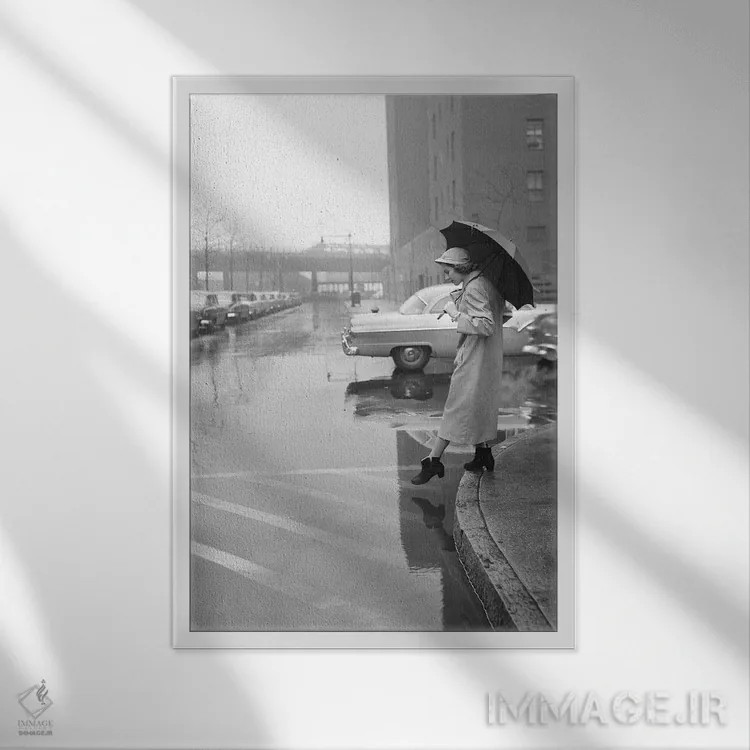 تابلو دکوراتیو دهه ۱۹۵۰ زن با بارانی، کلاه و چکمه، چتر به دست در حال عبور… اثر تصاویر وینتج - نمای قابدار سفید