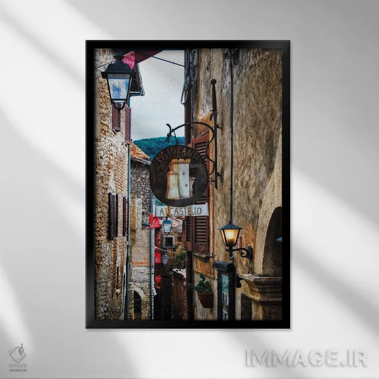 تابلو دکوراتیو خیابان باریک قرون وسطایی با تابلوها و چراغ ها، سرمونتا، ایتال… اثر جورج اوزه - نمای قابدار مشکی