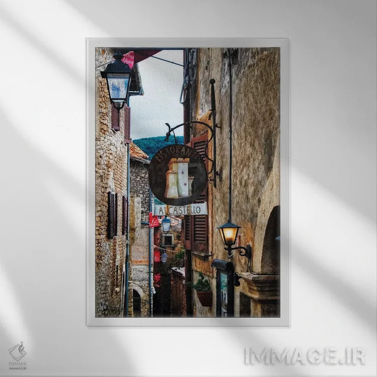 تابلو دکوراتیو خیابان باریک قرون وسطایی با تابلوها و چراغ ها، سرمونتا، ایتال… اثر جورج اوزه - نمای قابدار سفید